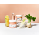 Two white tubs of Radeq Lab sugar paste with peach-colored labels are displayed on a white surface against a peach background, styled with natural ingredients including a corn cob, a turnip, and a green leafy vegetable in clear glass containers.